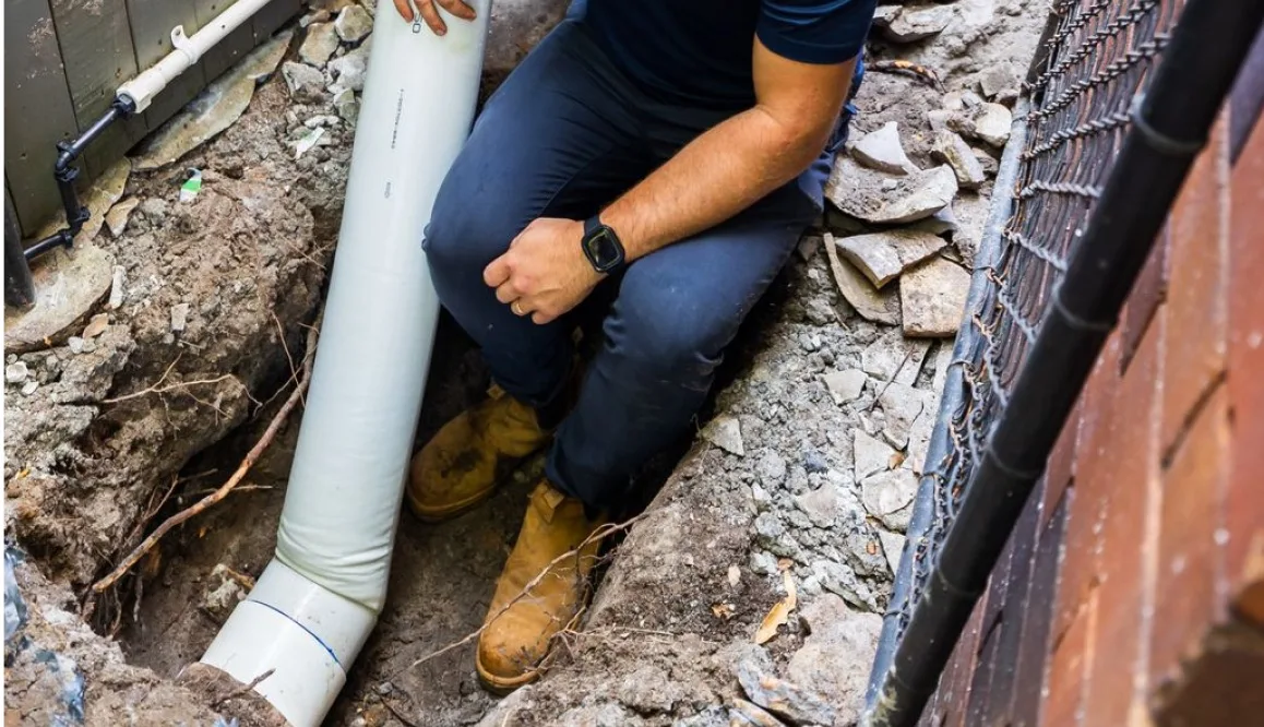 Plumber installing a new PVC drain line in an open trench